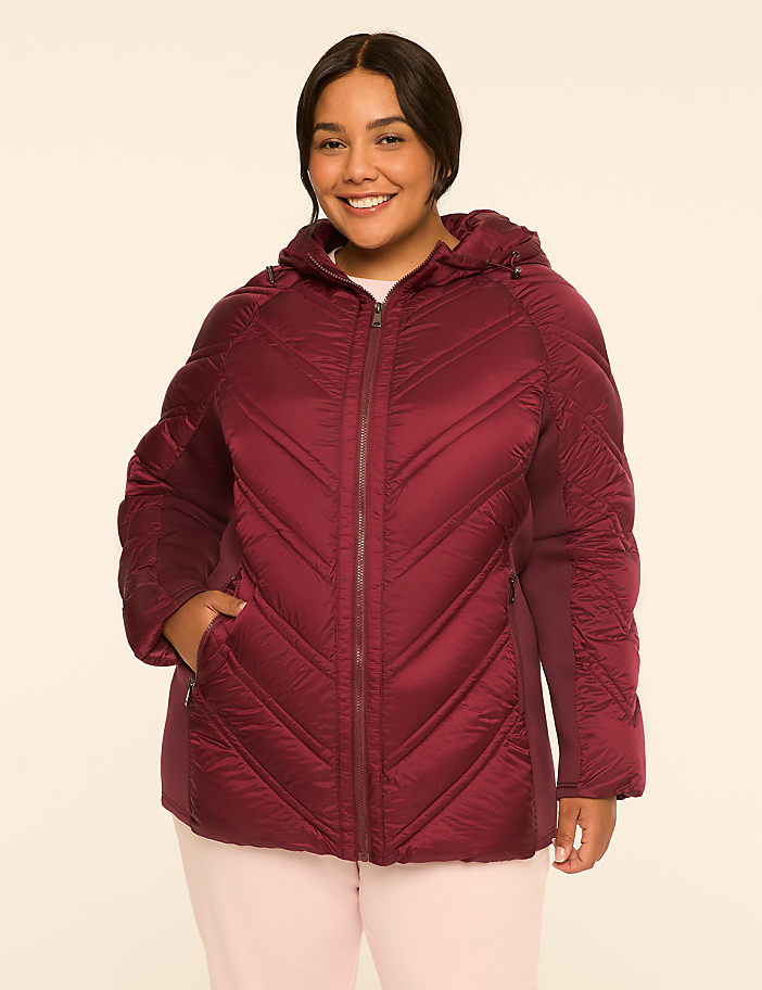 A smiling woman in a burgundy puffer jacket stands against a plain, light-colored background.