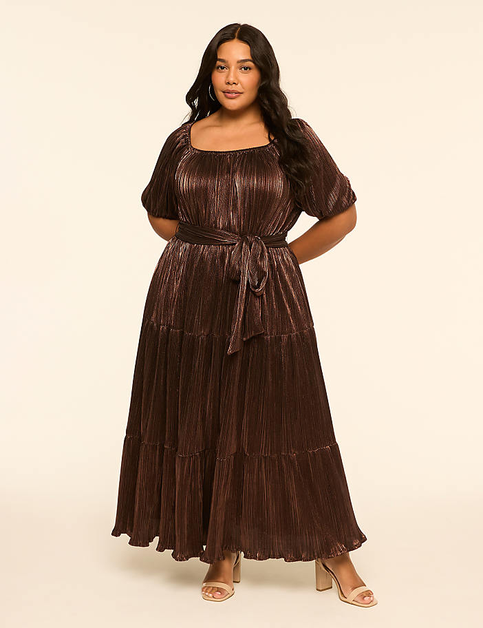 A woman in a shimmering brown tiered dress stands against a plain, light-colored background.
