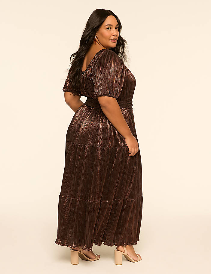 A woman in a shimmering bronze dress stands against a plain, light-colored background.