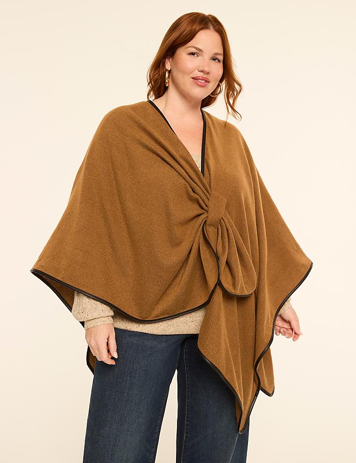 A woman in a brown poncho with a knot detail stands against a plain, light-colored background.