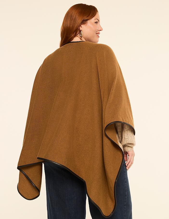 A woman in a brown poncho with leather trim stands against a plain, light-colored background.