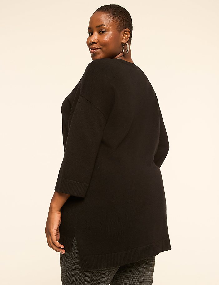 A woman in a black sweater and patterned pants stands against a plain, light-colored background.