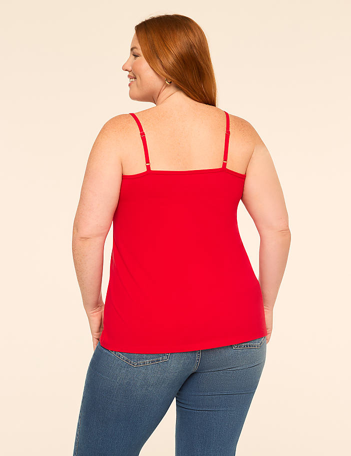 A woman in a red camisole and blue jeans stands against a plain, light-colored background.