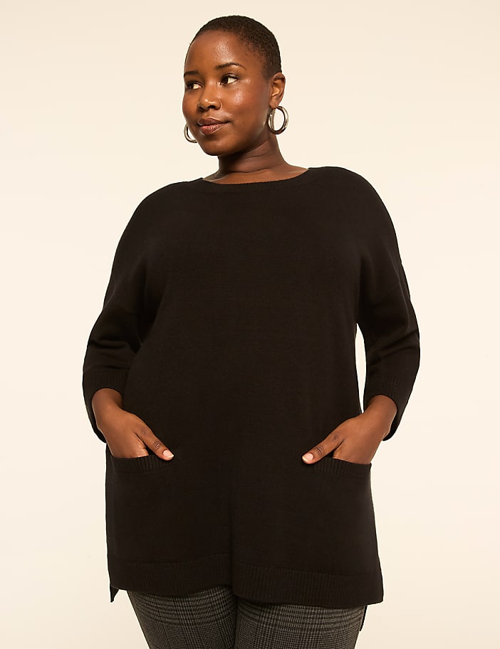A woman in a black sweater with pockets stands against a plain, light background.