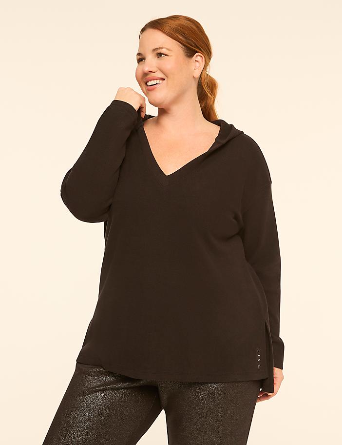 A smiling woman in a black hoodie and sparkly pants stands against a plain, light-colored background.