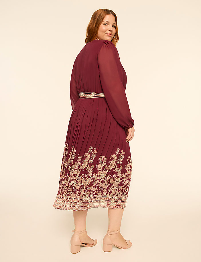 A woman in a burgundy dress with a floral hem stands against a plain, light-colored background.