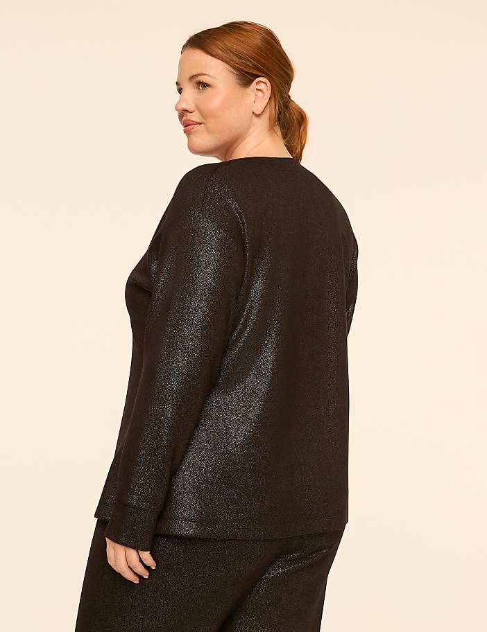 A woman with auburn hair stands in profile, wearing a shimmering black top and pants against a plain, light-colored background.
