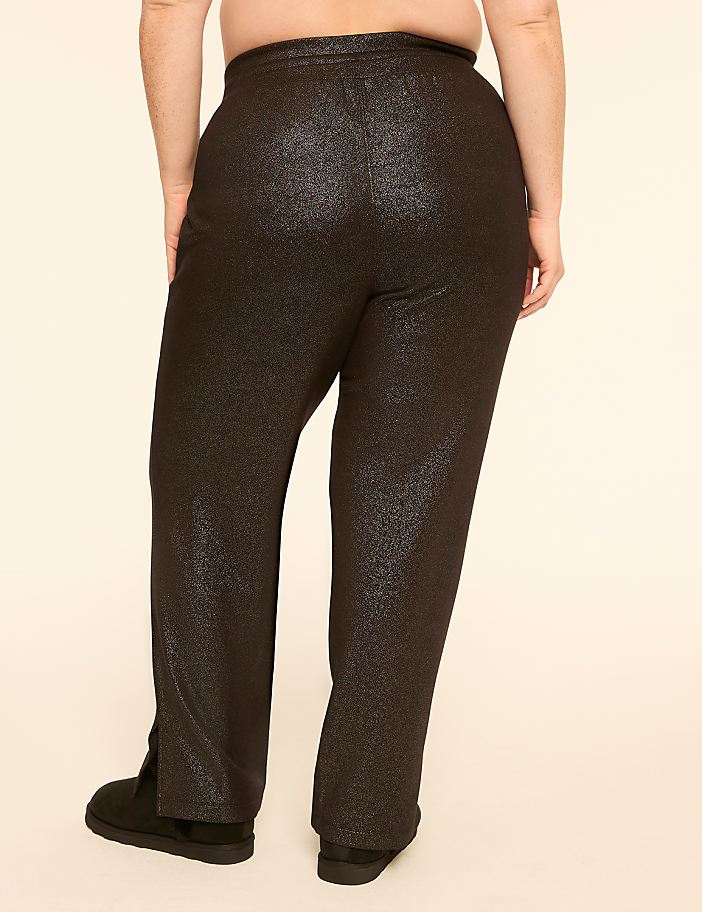 A person wearing sparkly black pants and black shoes stands against a plain, light-colored background.