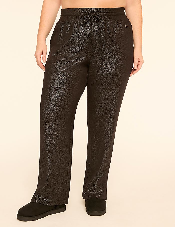 A person wearing sparkly black sweatpants and black slippers stands against a plain, light-colored background.