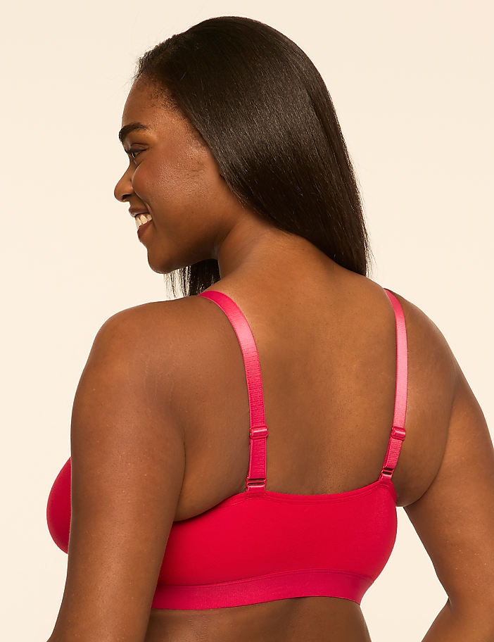 A woman in a red bra smiles over her shoulder against a plain, light-colored background.