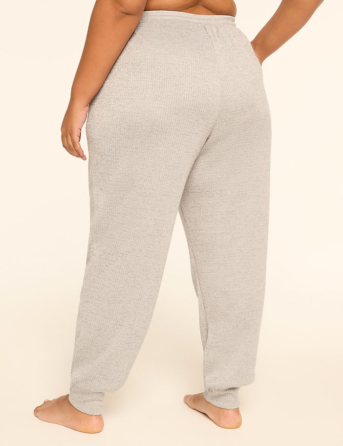 A person wearing grey sweatpants stands with their back to the viewer against a plain, light-colored background.