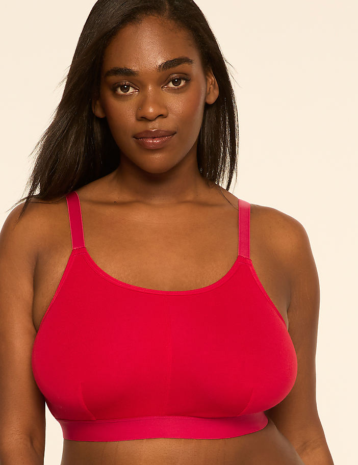 A woman with dark hair and brown eyes wears a red bra against a plain, light-colored background.