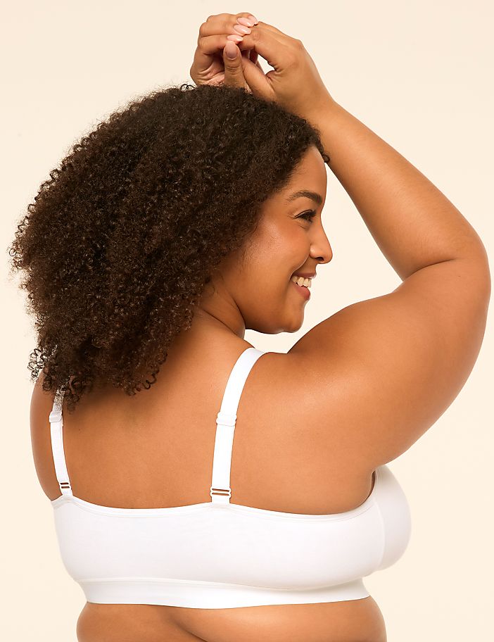 A smiling woman with curly hair in a white bra is shown from the back against a plain, light-colored background.