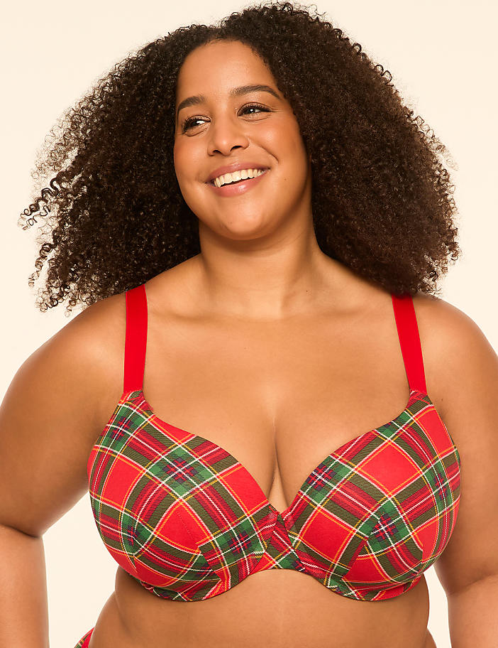 A smiling woman with curly hair wears a red plaid bra with red straps against a plain, light background.