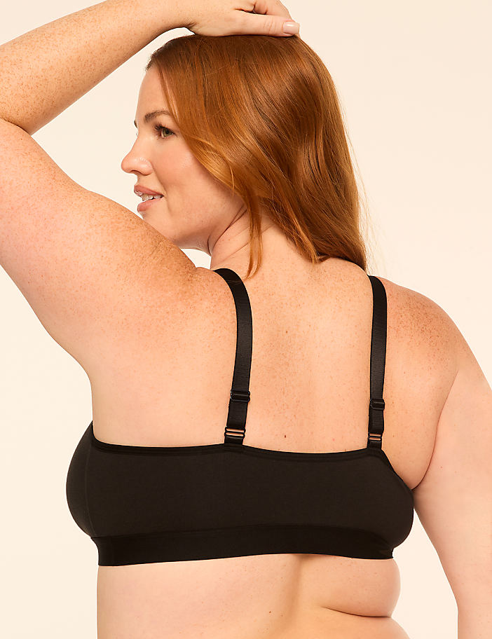A woman with red hair and freckles, wearing a black bra, is shown from the back against a plain, light-colored background.