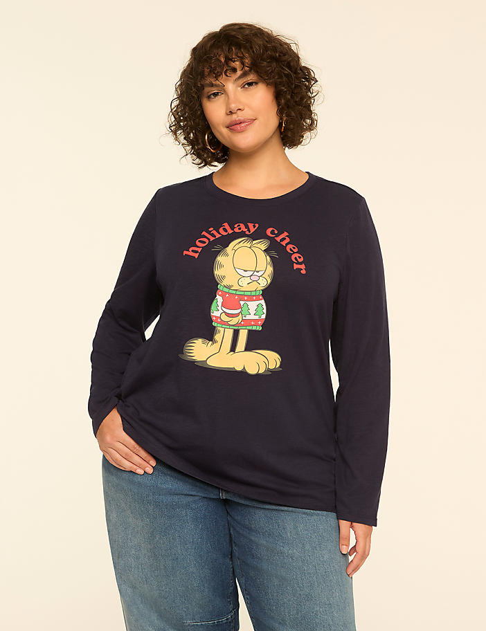 A woman in a navy blue long-sleeved shirt with a Garfield holiday graphic stands against a plain cream background.