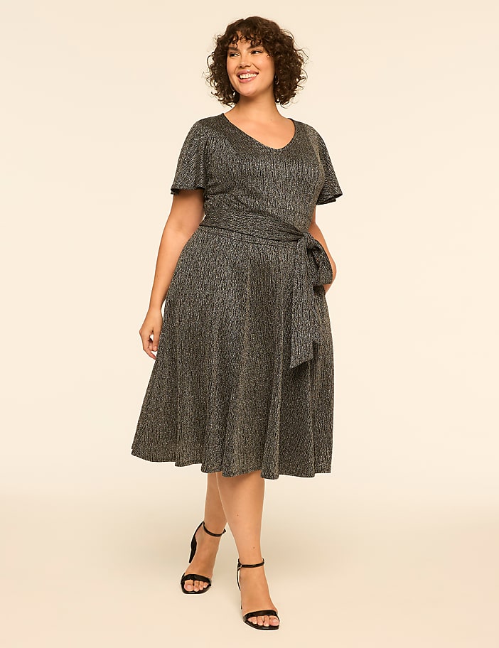 A woman in a sparkly grey wrap dress stands on a plain beige background.