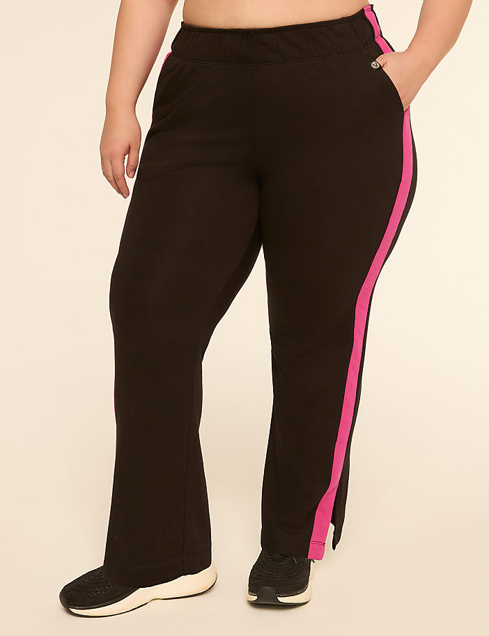 A person wearing black athletic pants with a pink stripe down the side stands against a plain, light-colored background.