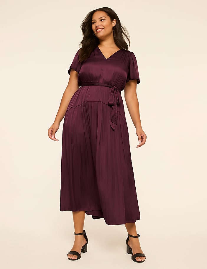 A woman in a burgundy dress stands against a plain, light-colored background.