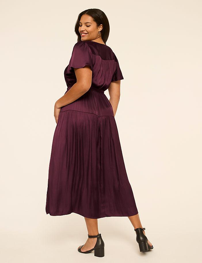 A woman in a burgundy dress poses against a plain, light-colored background.
