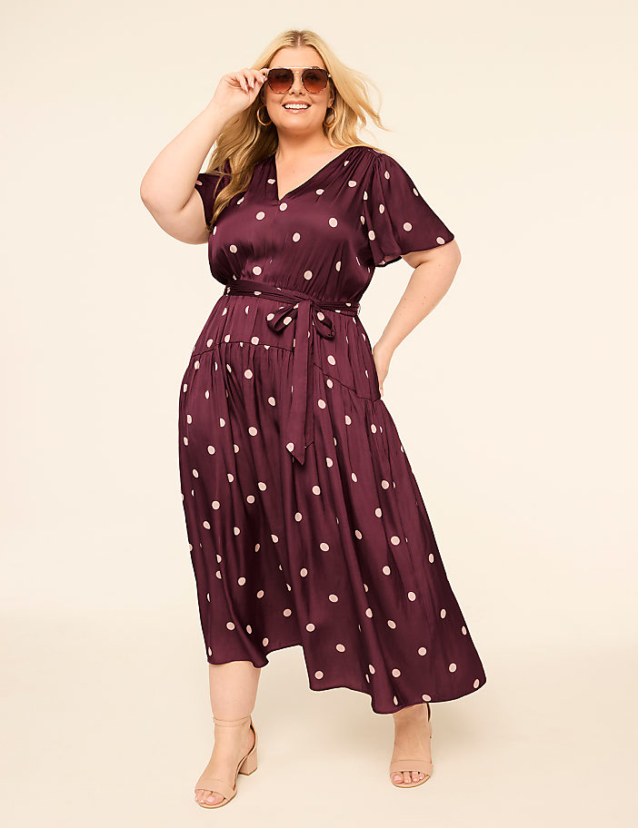 A smiling woman in a polka-dot dress poses against a plain, light-colored background.