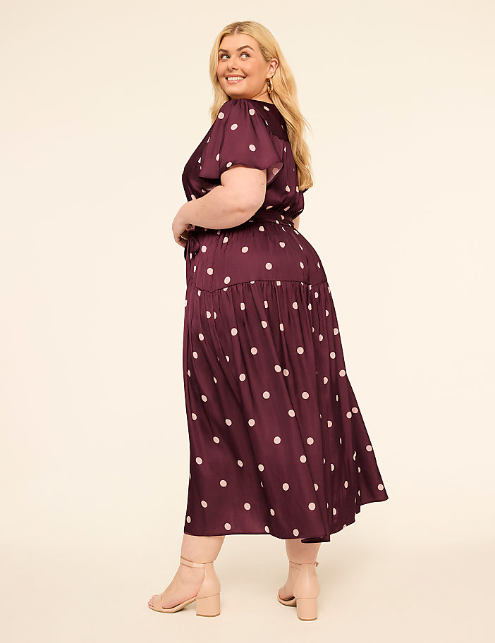 A woman in a polka-dot dress poses against a plain, light-colored background.