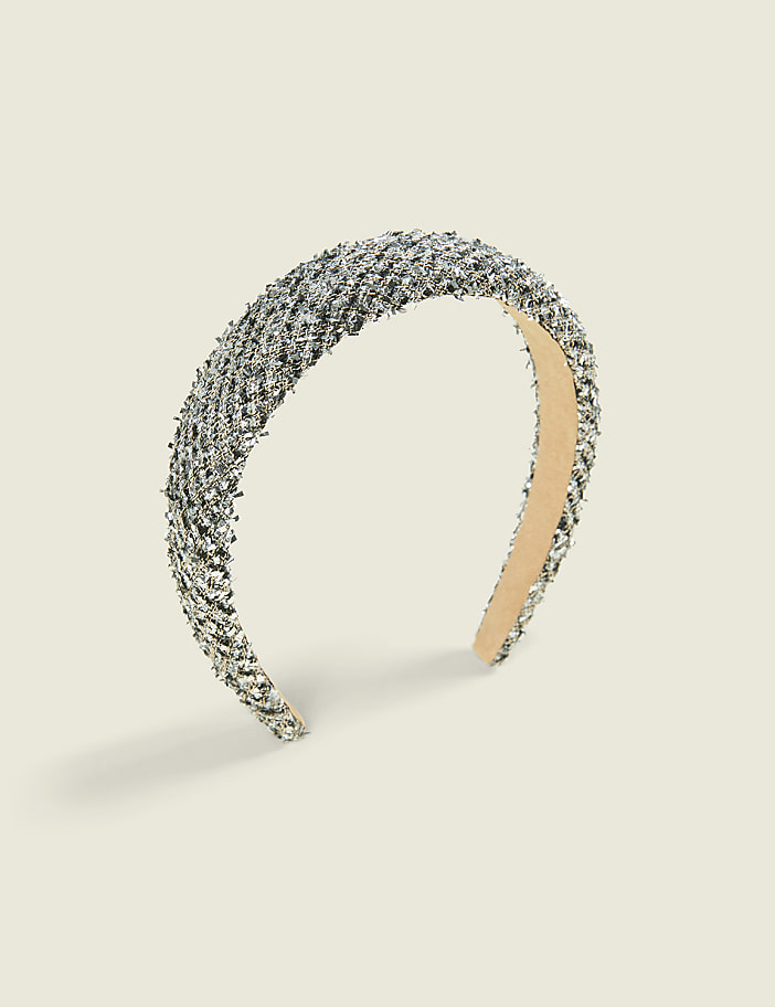 A silver glittery headband sits centered against a plain, light beige background.