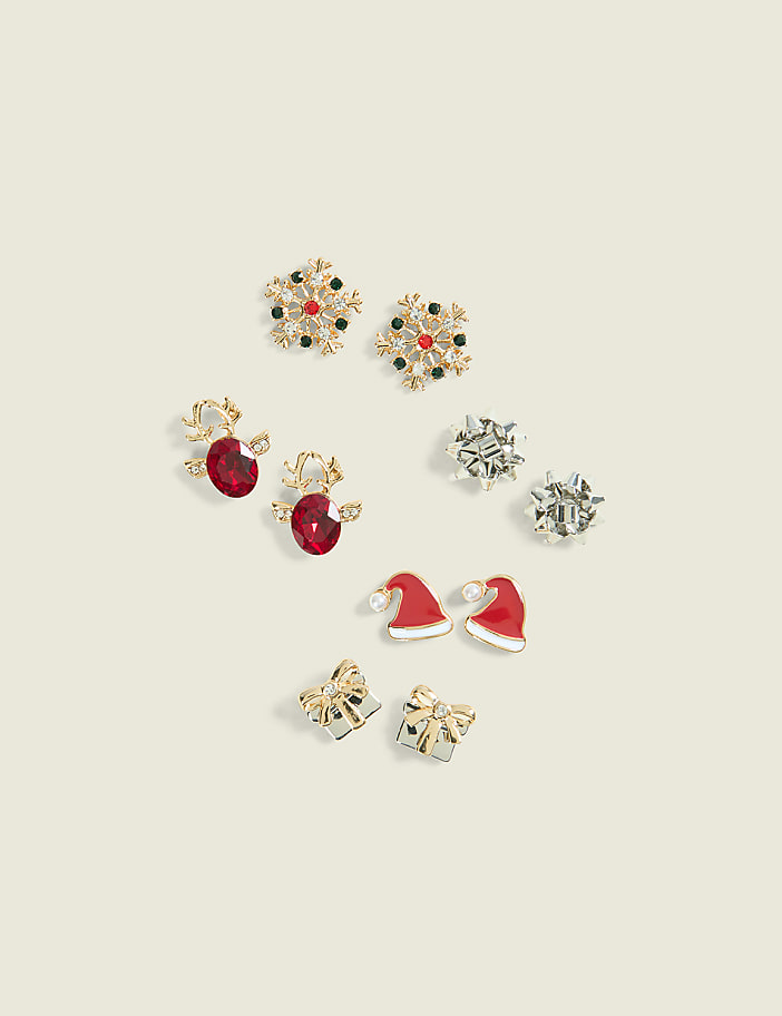 Five pairs of festive holiday-themed stud earrings are scattered across a plain, light beige background.