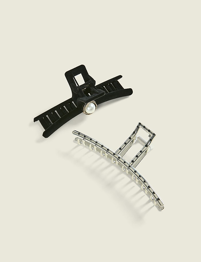 A black velvet hair claw with a pearl accent and a silver metallic hair claw are positioned on a plain, light-beige background.