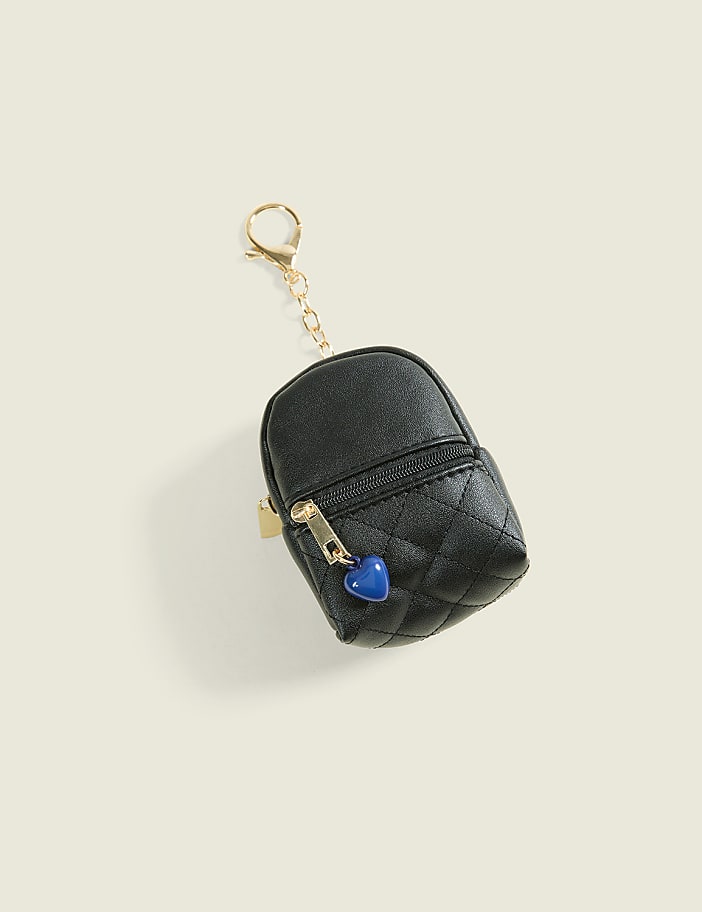 A small, black quilted coin purse with a blue heart charm and gold hardware sits against a plain, light-colored background.