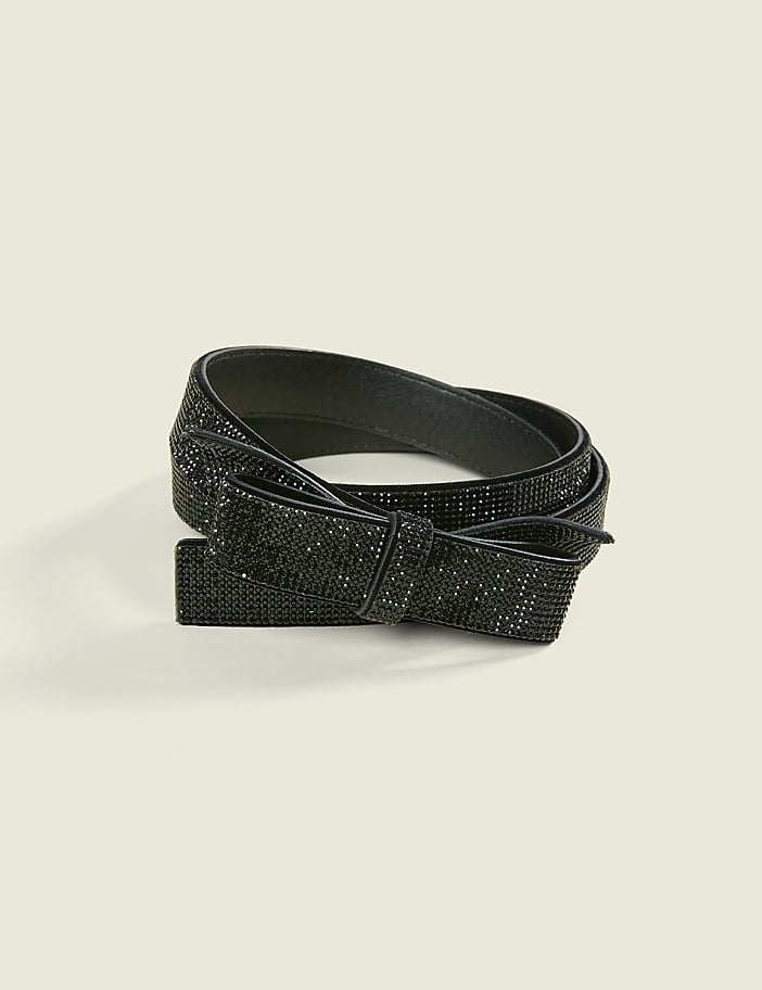 A sparkling black rhinestone belt with a bow detail rests on a plain, light beige background.