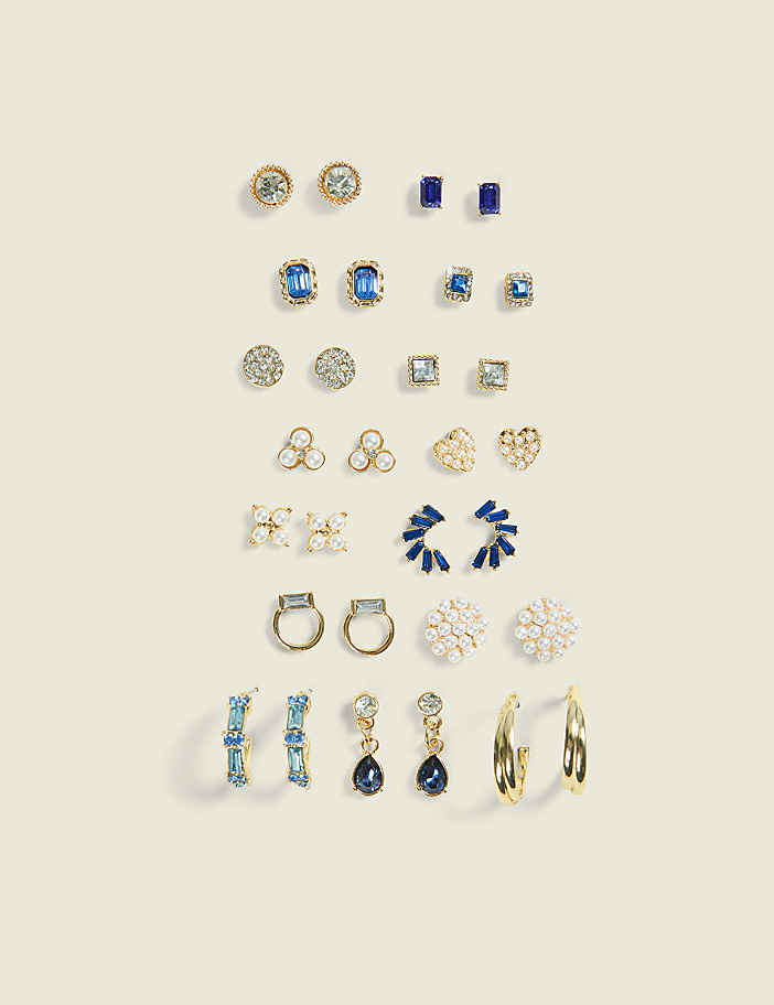 Various pairs of gold and gemstone earrings are arranged in neat rows against a plain, light beige background.
