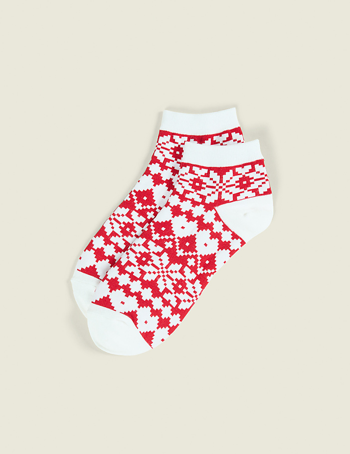 A pair of white socks with red Fair Isle patterns lies on a plain, light beige background.