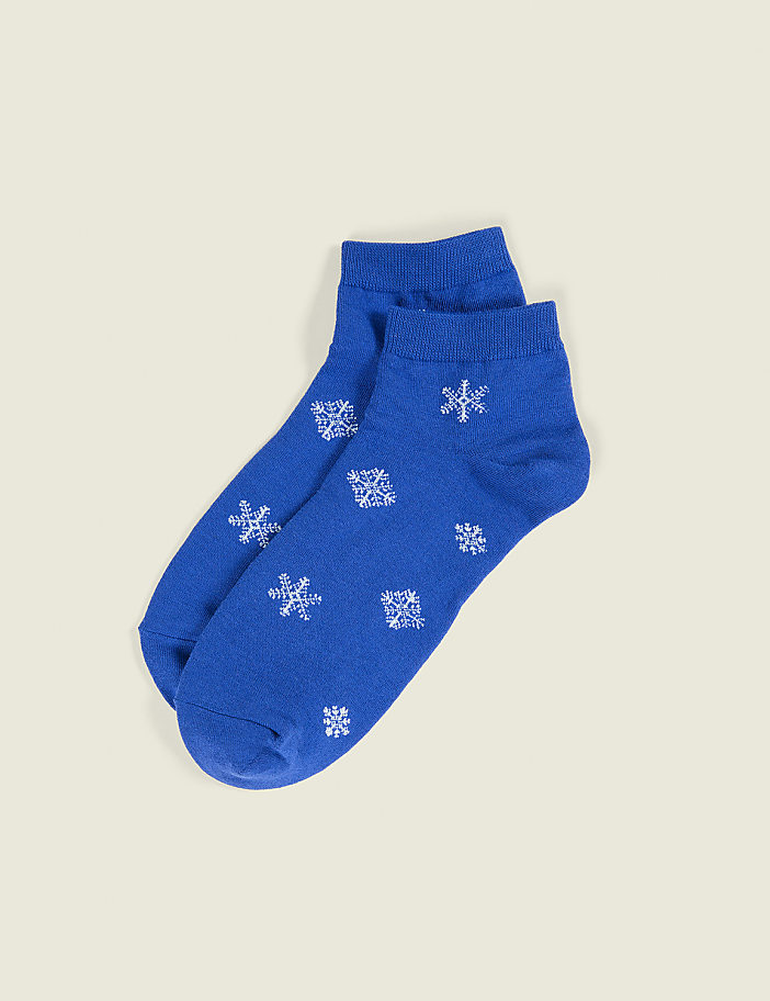A pair of blue socks with white snowflake patterns lies on a plain, light beige background.