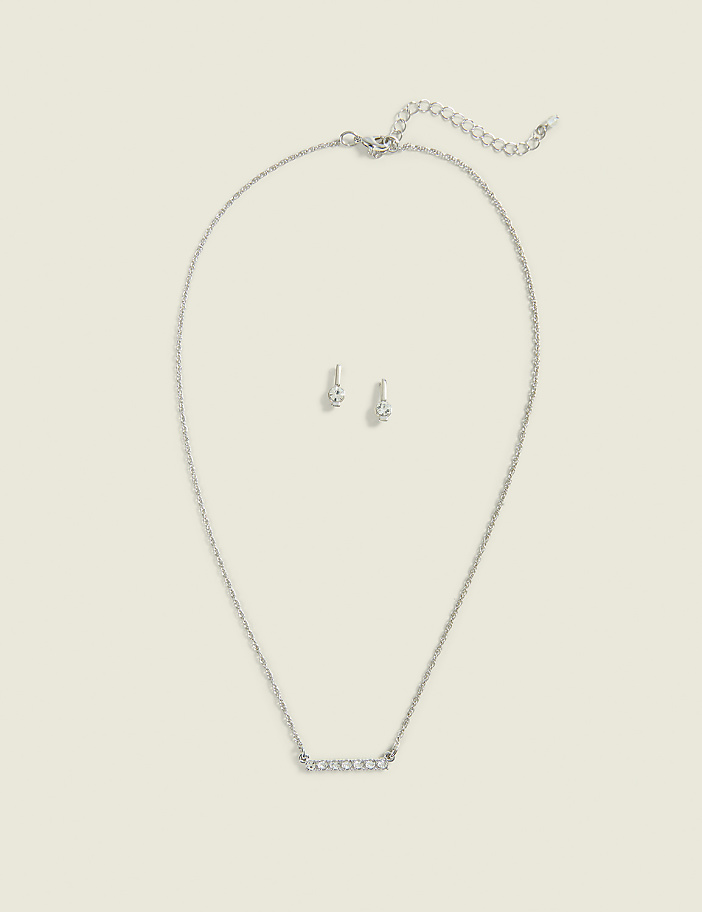 A silver necklace with a bar pendant and matching stud earrings are laid out against a plain, light beige background.