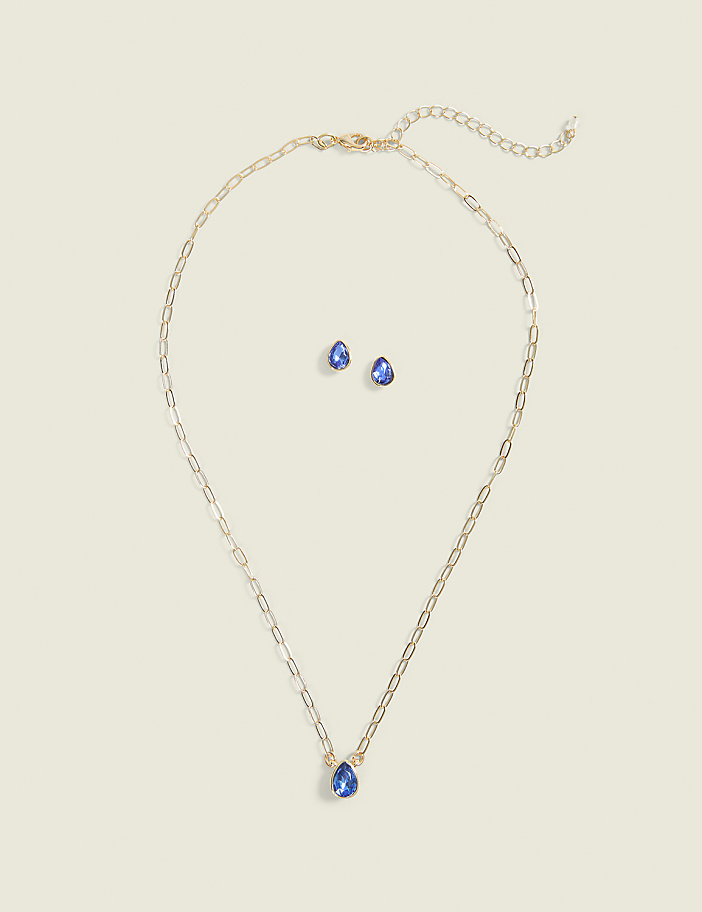 A gold chain necklace with a blue teardrop pendant and matching stud earrings are set against a plain, light beige background.