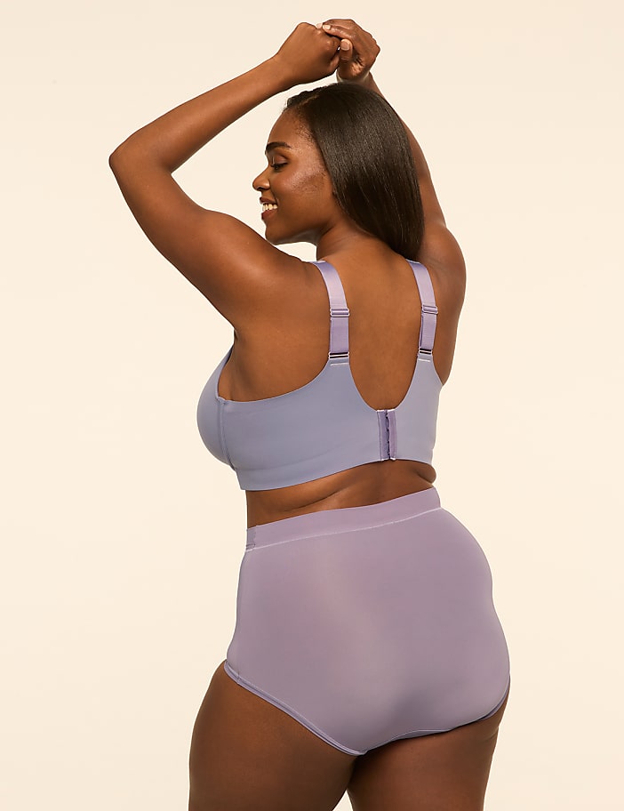 A woman wearing a purple lingerie set poses with her arms raised against a plain, light-colored background.