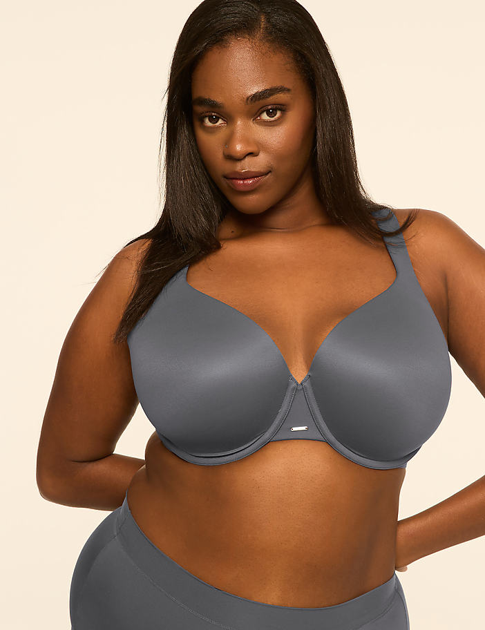 A woman wearing a grey bra and matching underwear stands against a plain, light-colored background.
