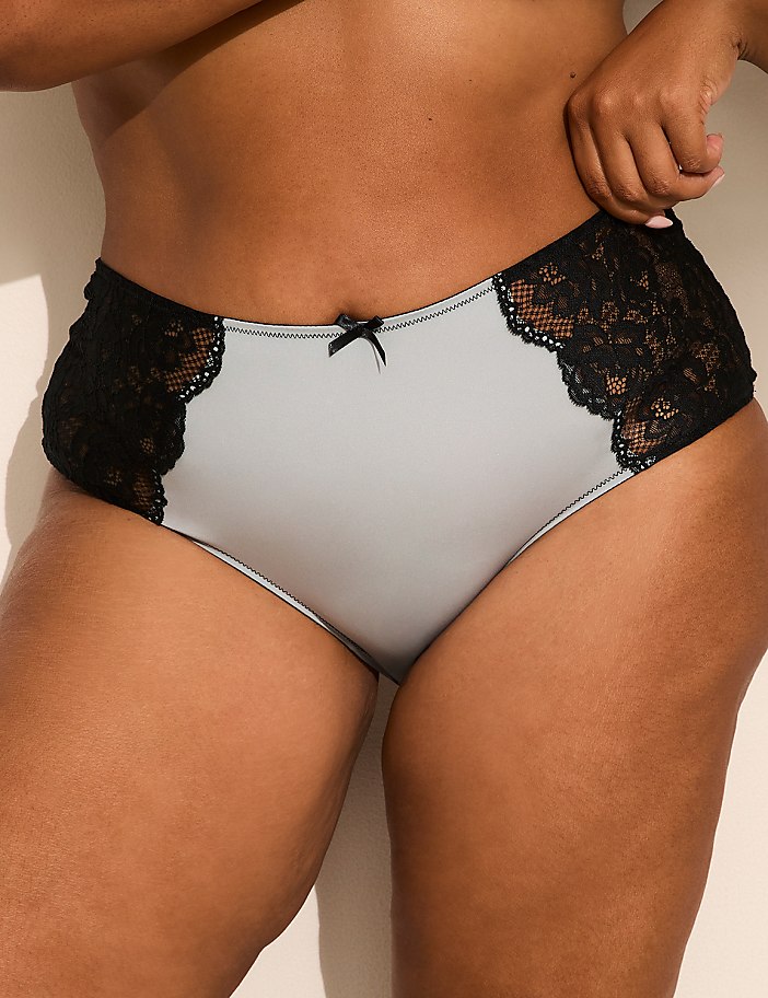 A person wears light grey panties with black lace side panels against a plain, light-colored background.