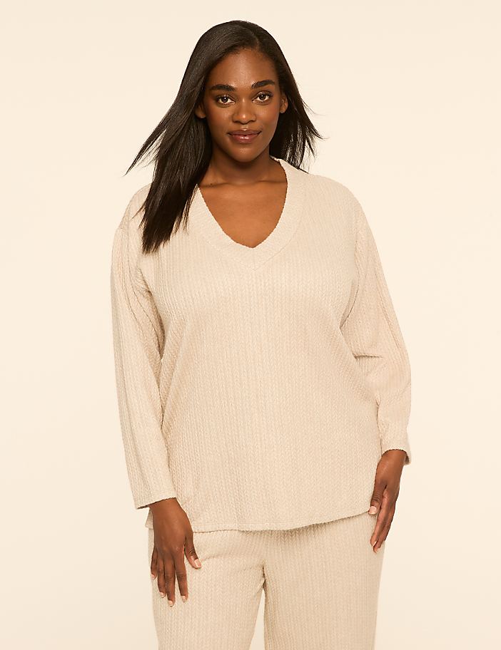 A woman wearing a beige ribbed lounge set stands against a plain, light-colored background.