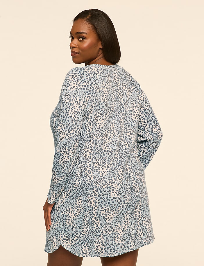 A woman wearing a blue and white leopard print tunic stands against a plain, light-colored background.