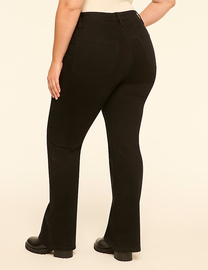 A person wearing black flared pants and black boots stands against a plain, light-colored background.