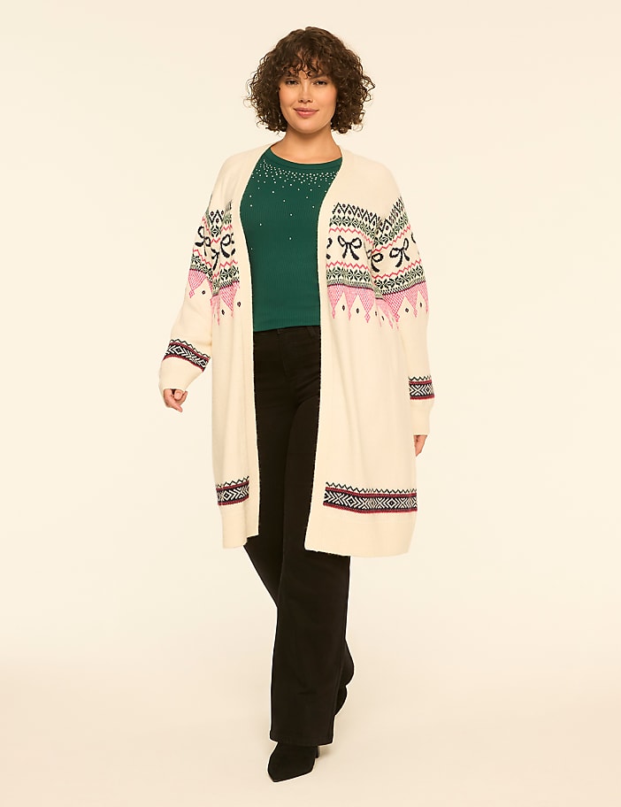 A woman wearing a long cream cardigan over a green top and black pants stands against a plain white background.