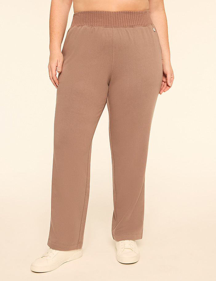 A person wears brown wide-leg pants and white sneakers against a plain, light-colored background.