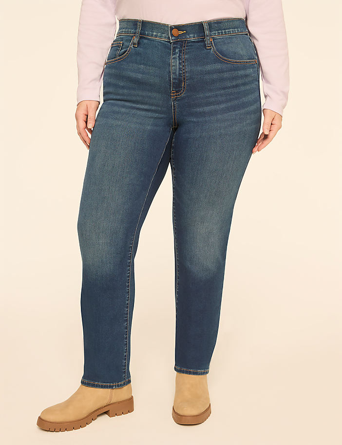 A person wearing a light purple top, blue jeans, and tan boots stands against a plain, light-colored background.