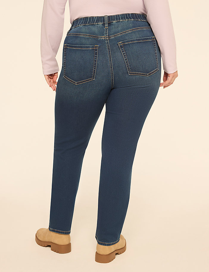 A person wearing a light purple top, blue jeans, and tan boots stands against a plain, light-colored background.