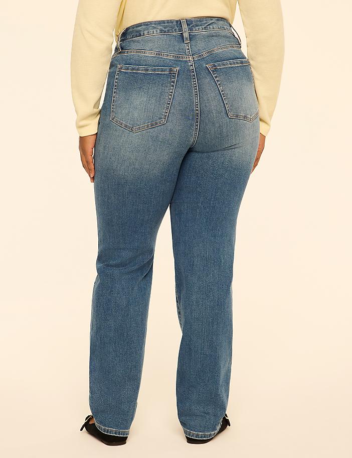 A person wearing blue jeans and a cream-colored top stands against a plain, light-colored background.