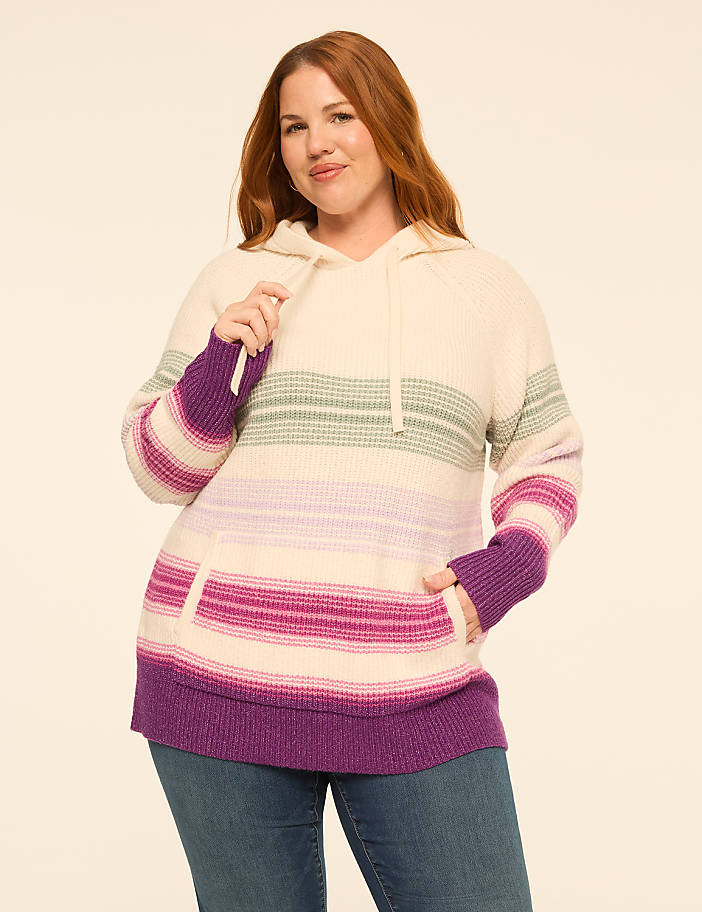 A woman wearing a striped purple and cream hoodie and blue jeans stands against a plain off-white background.