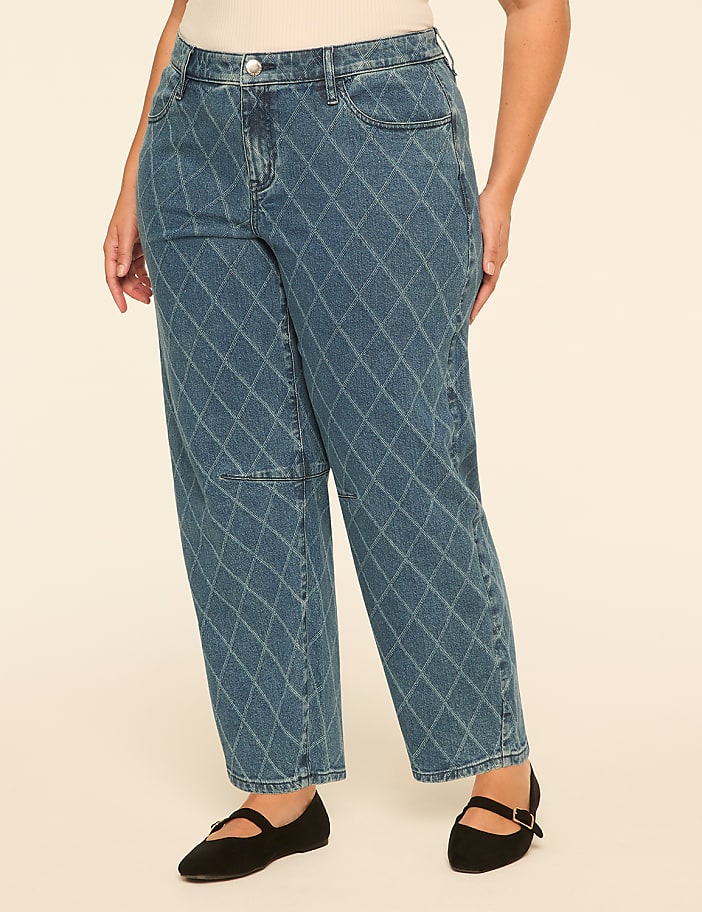 A person wears blue diamond-patterned jeans and black flats against a plain, light-colored background.