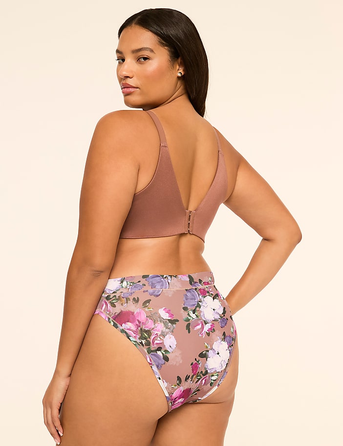 A woman wearing a brown bra and floral-print panties stands against a plain, light-colored background.